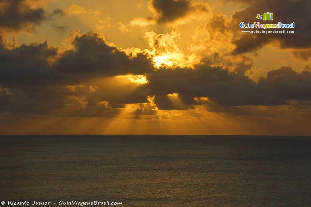 Imagem do sol se pondo atrás das nuvens e embaixo o mar, da Praia do Boldro, em Fernando de Noronha, Pernambuco, Brasil.